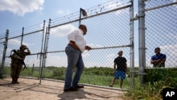 Hugo Urbina, center, talks through his fence to migrants who crossed the Rio Grande illegally at his pecan farm, Heavenly Farms, Friday, Aug. 26, 2022, in Eagle Pass, Texas. (AP Photo/Eric Gay)