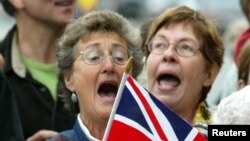 FILE - Christine Woolcott, left, and Theresa Kowall sing "God Save The Queen" outside Christ Church Cathederal in Victoria, British Columbia, while Queen Elizabeth II was attending services inside, Oct. 6, 2002. The anthem now will become "God Save the King."