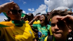 Pendukung Presiden Brazil Jair Bolsonaro melakukan salam hormat serta menyayikan lagu nasional dalam aksi protes menentang kekalahan Bolsonaro dalam pemilu presiden yang berlangsung bulan lalu. Aksi berlangsung di Brasilia, Brazil, pada 15 November 2022. (Foto: AP/Eraldo Peres)