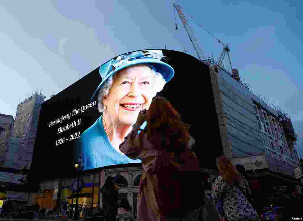 People takes photos of an image of Queen Elizabeth displayed at Piccadilly Circus in London, Sept. 8, 2022.