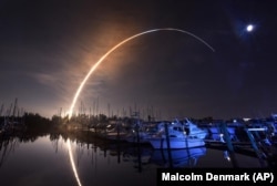 NASA's new moon rocket lifts off from the Kennedy Space Center in Cape Canaveral, Wednesday morning, Nov. 16, 2022, as seen from Harbor town Marina on Merritt Island, Fla. The moon is visible in the sky. (Malcolm Denemark/Florida Today via AP)