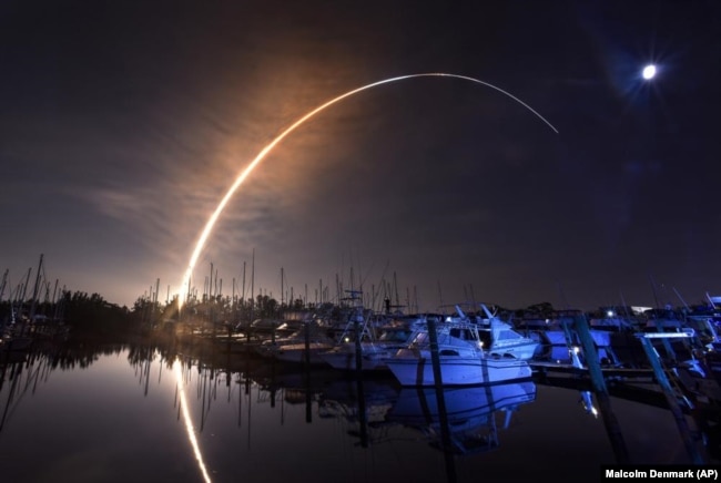 NASA's new moon rocket lifts off from the Kennedy Space Center in Cape Canaveral, Wednesday morning, Nov. 16, 2022, as seen from Harbor town Marina on Merritt Island, Fla. The moon is visible in the sky. (Malcolm Denemark/Florida Today via AP)