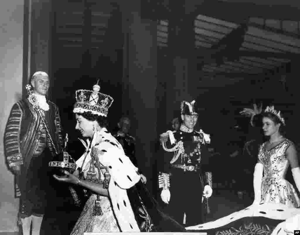 Ratu Inggris Elizabeth II mengenakan Mahkota Kerajaan berhiaskan berlian dan membawa Orb dan Tongkat Kerajaan dengan Salib, meninggalkan Westminster Abbey, London, pada akhir upacara penobatannya sebagai Ratu Inggris, 2 Juni 1953.&nbsp;