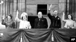 ARCHIVO - En esta foto de AP del 8 de mayo de 1945, la entonces princesa Isabel saluda desde un balcón del Palacio de Buckingham junto a su madre, la reina Isabel, el primer ministro Winston Churchill, su padre el rey Jorge VI y su hermana la princesa Margarita.
