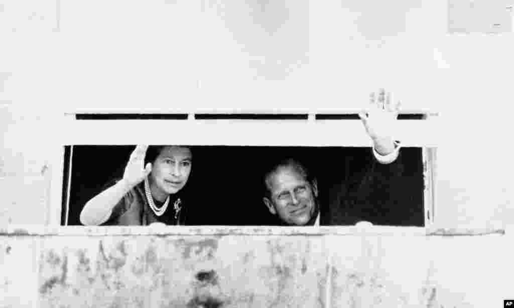 Queen Elizabeth II and her husband, Prince Philip, wave to a crowd of well-wishers, Aug. 10, 1977, from a partly closed window in Hillsborough Castle, 12 miles south of Belfast, Northern Ireland.