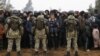 Belarusian service members stand guard as migrants gather for the distribution of humanitarian aid in a makeshift camp on the Belarusian-Polish border in the Grodno region on November 14, 2021. (Oksana Manchuk/BelTA/Handout via Reuters)