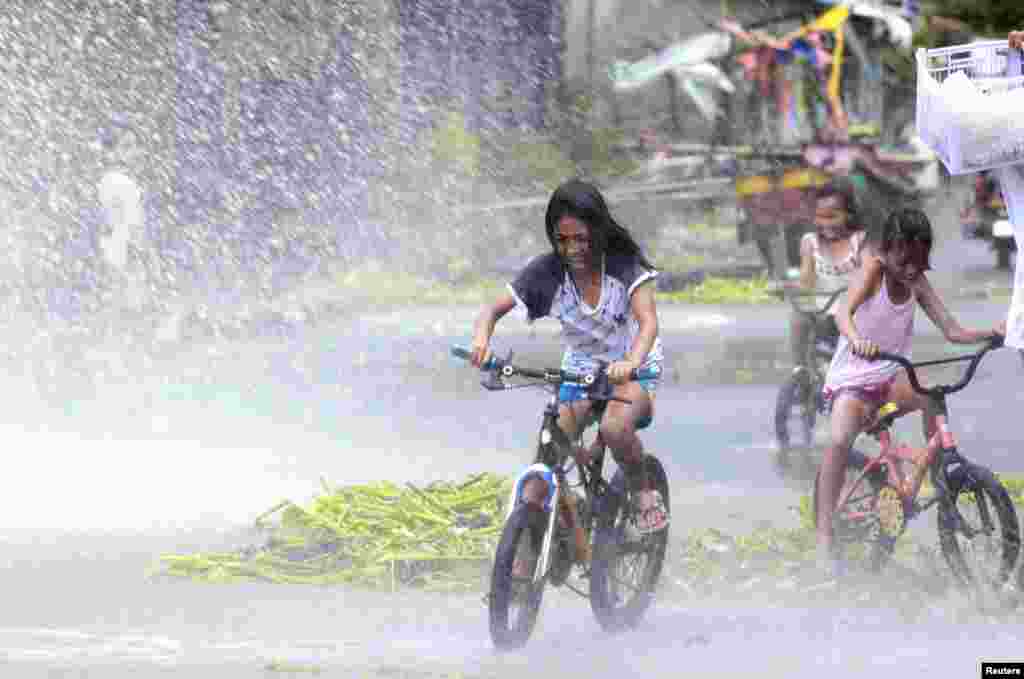 Anak-anak perempuan bersepeda di tengah percikan air dari ombak kuat di desa pesisir sebelah selatan Manila. (Reuters/Charlie Saceda)