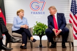 FILE - U.S. President Donald Trump, accompanied by German Chancellor Angela Merkel, left, speaks during a bilateral meeting at the G-7 summit in Biarritz, France, Aug. 26, 2019.