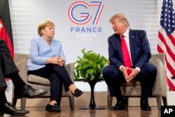 FILE - U.S. President Donald Trump, accompanied by German Chancellor Angela Merkel, left, speaks during a bilateral meeting at the G-7 summit in Biarritz, France, Aug. 26, 2019.