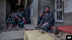 In this April 18, 2017 photo, Kashmiri man Farooq Ahmed Dar, right, sits along with her mother as school children watch from distance at his residence in Chill village, about 60 Kilometers (38 miles) southwest of Srinagar, Indian controlled Kashmir. 