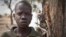 In this photo taken Saturday, Feb. 15, 2014, Ajing Abiik, 12, who fled from his hometown of Bor when the fighting broke out in December, stands next to the tree where he and his two brothers sleep in Minkaman IDP camp, Awerial County, in South Sudan. The 