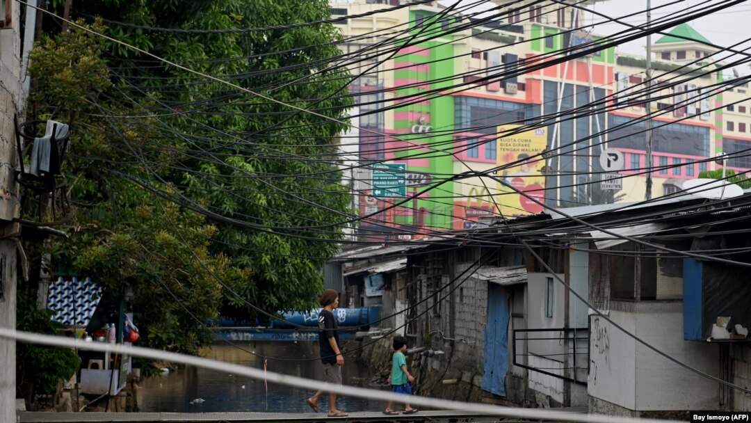Seorang pria dan anak laki-laki melintasi jembatan kecil buatan masyarakat yang tinggal di bantaran sungai di Jakarta pada 26 November 2019. (Foto: AFP/Bay Ismoyo)