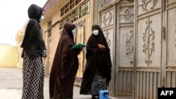 FILE - Afghan woman health workers wait by the door outside a house to administer Oral poliovirus vaccines (OPV) to the residing children during an immunisation campaign in Herat, May 15, 2023.