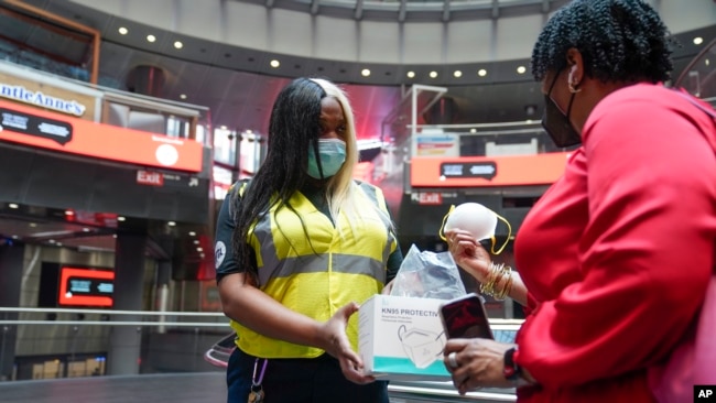 MTA employee Shanita Hancle, left, hands out masks to commuters at the entrance to a subway station in New York, June 8, 2023. Air pollution from Canadian wildfires are cloaking the northeastern U.S. for a second day.