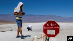 People cover themselves in white towels as they walk around Badwater Basin in Death Valley National Park, California, July 7, 2024. Forecasters say a heat wave could break previous records across the U.S. 