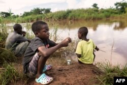 FILE—Two boys and a man fish in a river in Mtandile in Lilongwe, on February 20, 2023 in an area that has been highly affected by the cholera outbreak due to scarce access of clean drinking water.