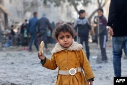 A Palestinian girl eats a piece of bread as people check debris on Feb. 22, 2024, following overnight Israeli air strikes in Rafah refugee camp in the southern Gaza Strip.