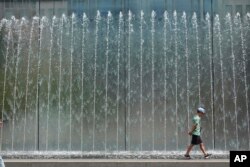 A boy walks on the edge of a fountain in Milan, Italy, Wednesday, July 19, 2023. An intense heat wave has reached Italy, bringing temperatures close to 40 degrees Celsius in many cities across the country.