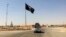 FILE - A vehicle passes by a flag of the Islamic State group in central Rawah, 281 kilometers northwest of Baghdad, Iraq. 