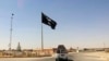 FILE - A vehicle passes by a flag of the Islamic State group in central Rawah, 281 kilometers northwest of Baghdad, Iraq. 