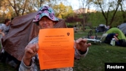 FILE : A homeless woman holds up a notice a police officer gave her giving her 72 hours to move her tent from the park, in Grants Pass, Oregon, April 18, 2024. 