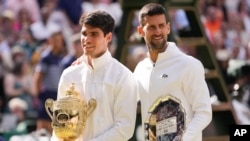 Carlos Alcaraz dari Spanyol (kiri) memegang trofi juara tunggal putra Wimbledon bersama Novak Djokovic dari Serbia usai final tunggal putra di kejuaraan tenis Wimbledon di London, Minggu 14 Juli 2024.