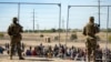 ARCHIVO - Migrantes esperan en fila junto a la valla fronteriza bajo la vigilancia de la Guardia Nacional de Texas para ingresar a El Paso, Texas, el 10 de mayo de 2023.
