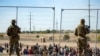 Sejumlah migran tampak menunggu di samping pagar pembatas yang dikawal oleh penjaga perbatasan Texas di el Paso, Texas, pada 10 Mei 2023. (Foto: AP/Andres Leighton)