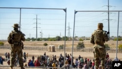 Sejumlah migran tampak menunggu di samping pagar pembatas yang dikawal oleh penjaga perbatasan Texas di el Paso, Texas, pada 10 Mei 2023. (Foto: AP/Andres Leighton)