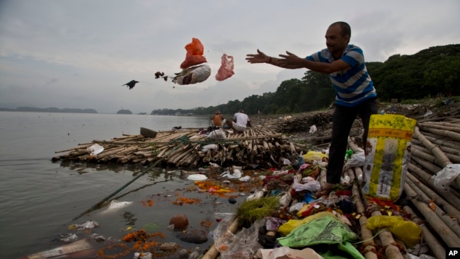 FILE - A Hindu devotee throws flowers and plastic bags into Brahmaputra river in Gauhati, India, Oct. 9, 2019. Negotiators at UNESCO in Paris discuss ways to end plastic pollution.