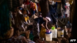 A woman cleans eating utensils near a burning stove surrounded by some of her belongings at a local church in the Delmas district of Port-Au-Prince, June 11, 2024.