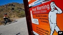 A cyclist finishes his ride early to beat high temperatures, Monday, July 10, 2023, in Phoenix. National Weather Service says Phoenix has had 10 consecutive days of 110 degrees or above. (AP Photo/Matt York)