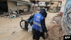 Seorang pria mengumpulkan sampah sambil mengenakan jaket berlogo Badan Bantuan dan Pekerjaan PBB untuk Pengungsi Palestina di Timur Dekat di sepanjang jalan di kota Jenin di Tepi Barat yang diduduki pada 30 Januari 2024. (Foto: AFP )
