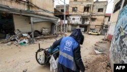 Seorang pria yang menggunakan jaket dengan logo UNRWA mengumpulkan sampah di jalanan Kota Jenin, Tepi Barat, pada 30 Januari 2024. (Foto: AFP/Jaafar Ashtiyeh)