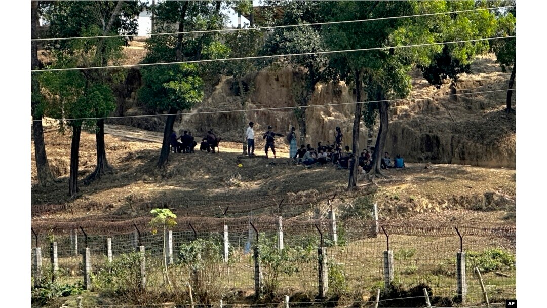 FILE - Members of Myanmar Border Guard Police, in civilian clothing, sit under the shade of trees after abandoning their posts following fighting between Myanmar security forces and Arakan Army as Bangladesh border guards stand guard in Bangladesh, Feb. 5, 2024.