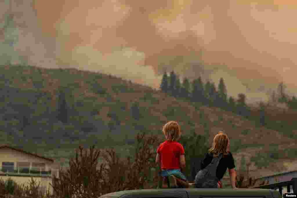 Locals gather to watch firefighting efforts amid heavy smoke from the Eagle Bluff wildfire in Osoyoos, British Columbia, Canada, July 30, 2023. The wildfire crossed the Canada-U.S. border from the state of Washington and prompted evacuation orders.