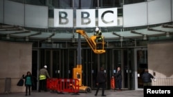 FILE - Repairmen work next to a sign at the British Broadcasting Corporation headquarters in London, March 13, 2023. The BBC is primarily funded by an annual television license set by the government and paid for by residents.