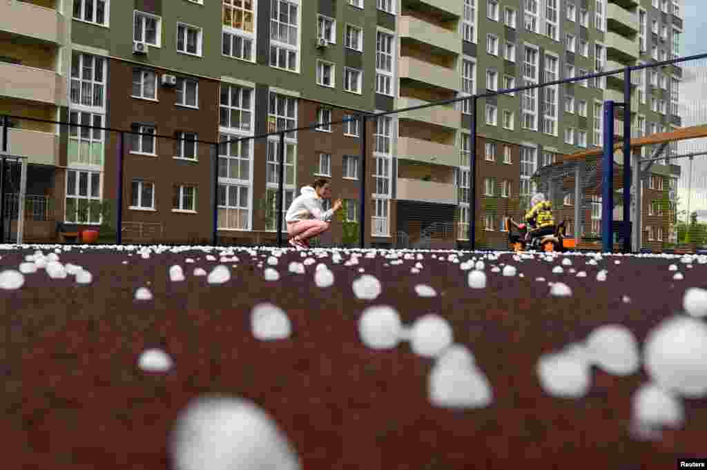A woman takes photos of a child on a sports ground covered with hailstones following a hail storm in the Siberian city of Omsk, Russia, June 27, 2023.