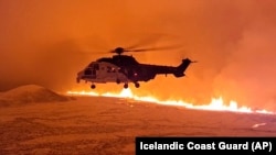 This image made from video provided by the Icelandic Coast Guard shows its helicopter flying near magma running on a hill near Grindavik on Iceland&#39;s Reykjanes Peninsula.