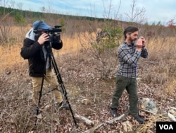 VOA videographer Adam Greenbaum, left, records Aston Bay Holdings CEO Thomas Ullrich as the geologist uses a hand lens to inspect a rock sample in Buckingham County, Virginia. (Steve Herman/VOA)