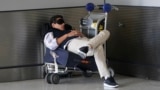 FILE - A traveler takes a nap as he waits for a ride outside Miami International Airport, Friday, July 1, 2022, in Miami. (AP Photo/Wilfredo Lee, File)