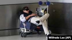 FILE - A traveler takes a nap as he waits for a ride outside Miami International Airport, Friday, July 1, 2022, in Miami. (AP Photo/Wilfredo Lee, File)