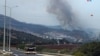 Un tanque israelí es transportado por una carretera, mientras se observa el humo del impacto de un proyectil lanzado desde el Líbano.