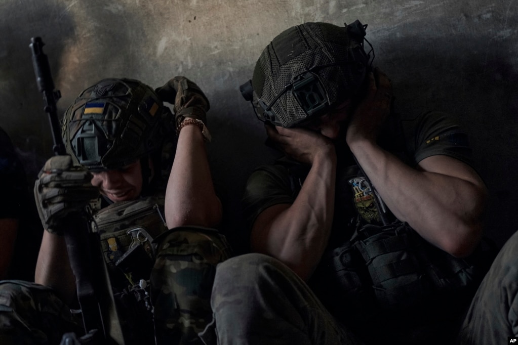 Soldados ucranianos se cubren los oídos para protegerse del ruido de los bombardeos rusos, en un refugio en el frente en la provincia de Zaporiyia, Ucrania, el 2 de julio de 2023. (AP Foto/Libkos).