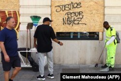 Seorang pekerja membersihkan pecahan kaca di samping sebuah papan yang bertuliskan "Keadilan untuk Nahel" di pusat kota Marseille, selatan Prancis, 1 Juli 2023. (Foto: Clement Mahoudeau/AFP)