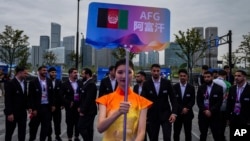 在中国杭州举行的第19届亚运会欢迎仪式上，一名志愿者举牌站在阿富汗塔利班政权派出的全部为男性运动员的队伍前。（2023年9月20日）