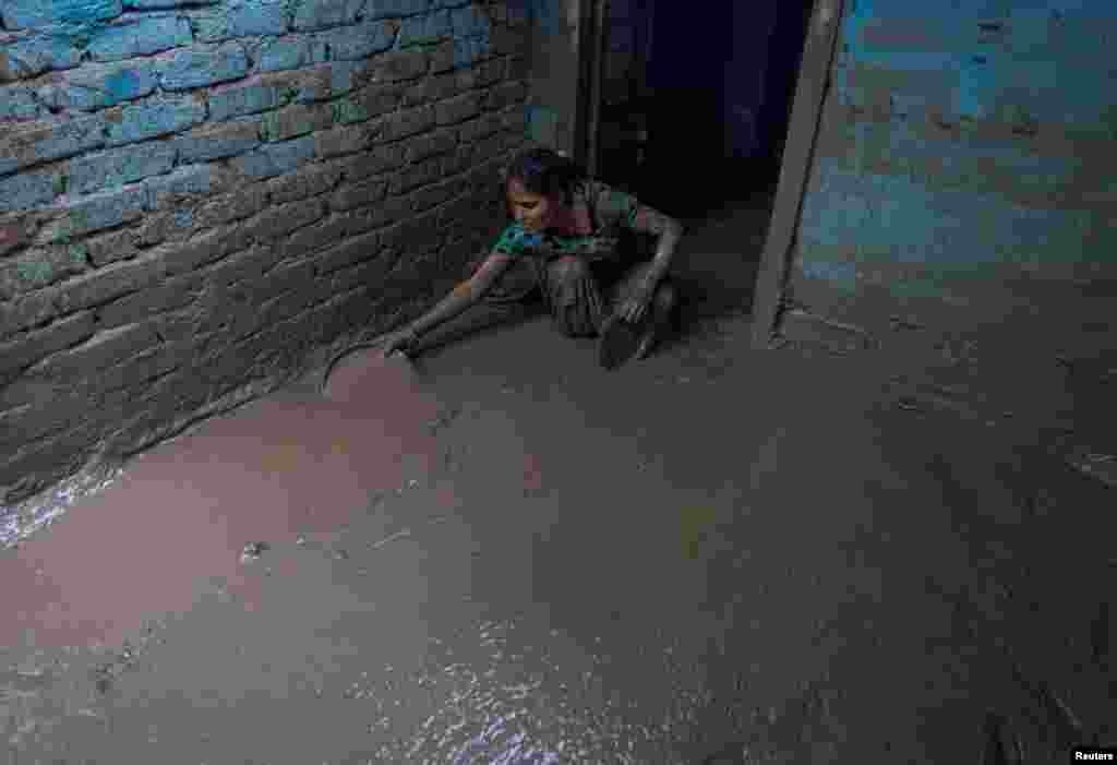 Munni Devi cleans the mud from the entrance of her house as flood water recedes from a residential area caused by overflowing of the river Yamuna following heavy rains, in New Delhi, India.