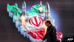 Seorang pria berjalan melintasi spanduk yang menampilkan gambar peluncuran rudal yang dihiasi dengan bendera Iran di pusat Teheran pada 15 April 2024. (Foto: AFP)