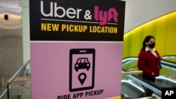 FILE - A passer-by walks past a sign offering directions to an Uber and Lyft ride pickup location at Logan International Airport, in Boston, Feb. 9, 2021. 