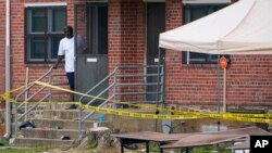 A person looks out the front door of a home as police tape surrounds the area of a mass shooting incident in the Southern District of Baltimore, July 2, 2023. 